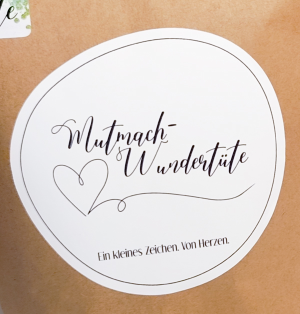 Mutmach-Wundertüte aus braunem Kraftpapier mit rundem Etikett und Herzillustration
